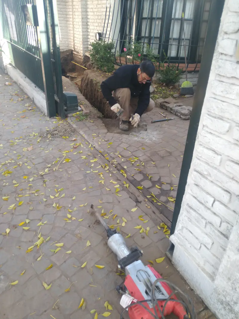 Especialista reparando cañería pluvial con martillo neumático en entrada de vivienda